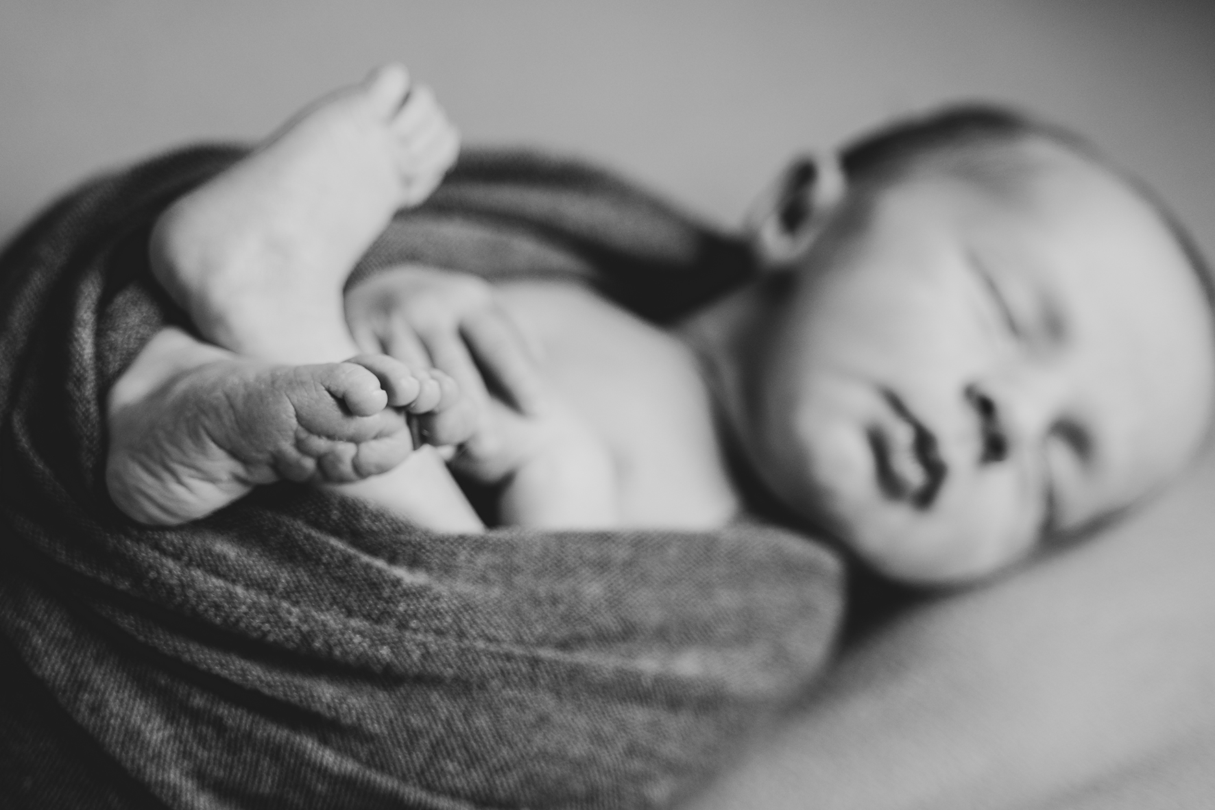 Detailbild der Babyfüße beim Babyshooting Neugeborenes Newbornfotos in schwarz weiß